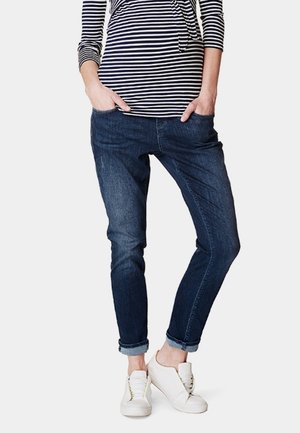 Donkerblauwe denim jeans met een relaxte pasvorm, voorzien van subtiele vervaging, frontzakken en opgerolde boorden, gecombineerd met witte sneakers.