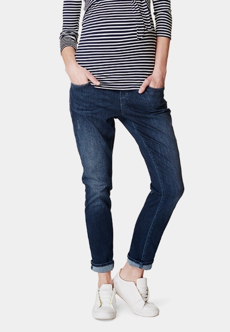 Mörkblå denimjeans med en avslappnad passform, med subtil blekning, framfickor och uppvikta fållar, kombinerat med vita sneakers.