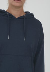 Mörkblå hoodie i mjukt material med en medellång design, framficka, dragsko och silverfärgade metalldetaljer.