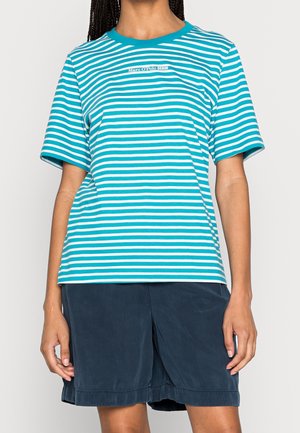 Persoon in een turquoise en wit gestreept T-shirt met korte mouwen en het logo "Marc O'Polo DENIM" en donkere blauw knielange shorts.