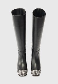 Mustad musta nahast kuni põlve kõrgused saapad, millel on ruudukujuline nina, hõbedaste nupukestega peapael ja lukupead välisküljel. Üldiselt sile tekstuur.