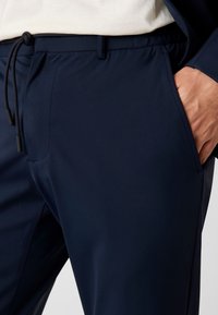 Marineblaue Jogginghose aus glattem Stoff mit elastischem Bund und verstellbarem Kordelzug. Verfügt über Seitentaschen und eine taillierte Passform.