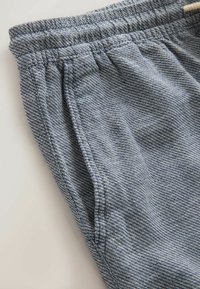 Gros plan sur un short en tissu texturé bleu et blanc avec une ceinture élastique et une poche latérale sur une surface claire.