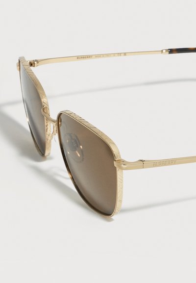 Γυαλιά ηλίου aviator με χρυσή κορνίζα, φακούς με καφέ απόχρωση και χαραγμένες λεπτομέρειες στις άκρες της κορνίζας και τους βραχίονες.