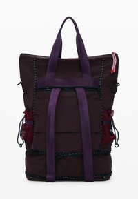 Lilla rygsæk med en tekstureret finish, der har justerbare stropper, netlommer på siderne og kontrasterende lynlåse. Kompakt, rektangulær form.