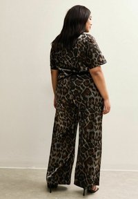 Completo in stampa leopardata con maniche corte e pantaloni a gamba larga, realizzato in un tessuto lucido, caratterizzato da una palette di colori scuri con tonalità di marrone e nero.