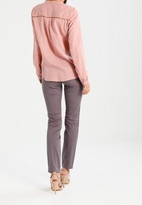 Blouse rose clair avec de légers pois, manches longues et détail de couture dans le dos, associée à un pantalon gris ajusté et des talons beiges.