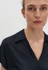Blouse bleu marine à col, avec un design en V, des manches courtes et une texture lisse. Le tissu semble léger et se drape légèrement.