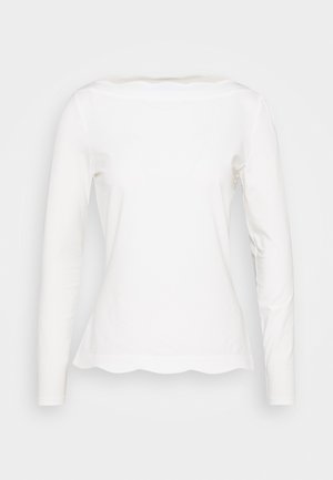 Chemise blanche à manches longues avec ourlet festonné et encolure bateau, présentée sur un fond uni.