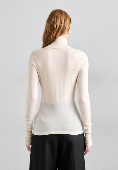 Gai krēms turtlenecks džemperis ar gludu, smalku adījumu. Tam ir garas piedurknes un nedaudz gradiēta efekts apakšmalā. Vienkāršs, minimālists dizains.