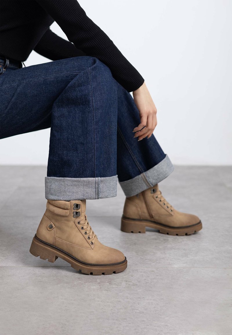 Botas de tobillo de cuero marrón claro con punta redondeada, cordones en el frente y suelas resistentes. Combinadas con jeans de mezclilla oscura, con los puños doblados en el dobladillo.