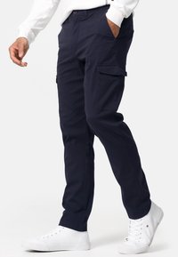 Pantalones cargo de color navy, hechos de algodón, con bolsillos laterales, un corte relajado y detalles de costura sutiles. Combinados con zapatillas blancas.