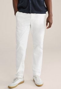 Hvide bukser med lige ben og en glat finish, båret sammen med en tekstureret marineblå cardigan. Fodtøjet har et hvidt design med gummisål.