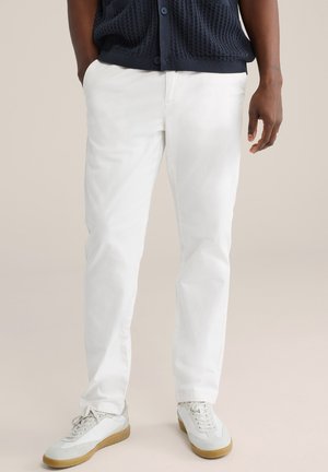 Witte, recht gesneden broek met een gladde afwerking, gedragen met een getextureerde marineblauwe cardigan. Schoeisel heeft een wit ontwerp met een gumkleurige zool.