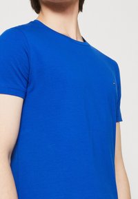 Blå t-shirt med korta ärmar, rund halsringning och en liten logotypdetalj på bröstet. Tillverkad av mjukt, slätt tyg.