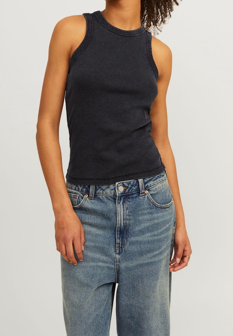 Débardeur noir côtelé sans manches porté avec un jean en denim bleu taille haute sur une personne aux cheveux bouclés.