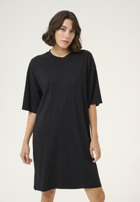 Svart oversized t-shirtklänning i mjuk bomull, rund halslinning, kortärmad, når mitt på låret, enkel design utan mönster eller detaljer.