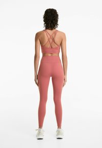 Sportbhar och leggins i en dämpad rosafärg, tillverkade av stretchigt material. Bh:n har korsande axelband; legginsen har en hög midja.