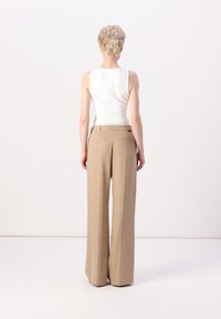 Witte mouwloze top en beige wijde broek. De outfit heeft een getailleerde silhouet en een soepele textuur, met een achterzakdetail.