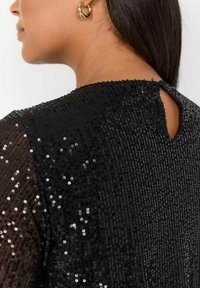 Svart paljett-topp med en texturerad yta, prydd med en nyckelhålsdetalj på baksidan och en rund halsringning. Elegant och glittrande finish.