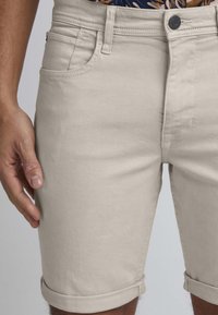 Lys beige denim shorts med slim fit. Har rullekanter, frontlommer og knaplukning. Glat tekstur og minimal søm.
