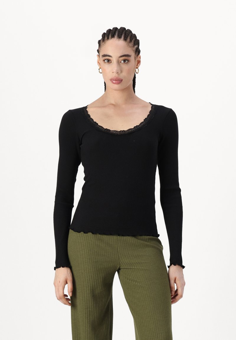 Top negru cu manșete lungi texturate, cu decolteu cu dantelă zimțată și manșete destrămate, asortat cu pantaloni verzi cu prindere lățită, texturați.
