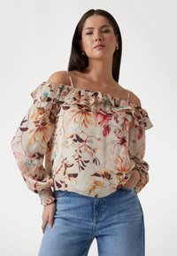 Floral off-shoulder blouse in light beige with ruffled neckline, long sleeves, and elastic cuffs; features colorful flower patterns.