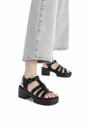 Las sandalias de plataforma negras cuentan con múltiples correas anchas, hebilla ajustable y suelas de goma texturizadas, complementadas por un diseño de tacón grueso.