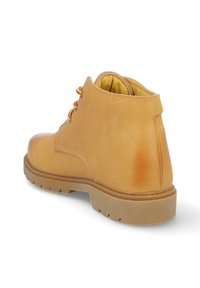 Bota de trabajo de cuero marrón claro con suela de goma gruesa y cordones a rayas rojos y amarillos, mostrada desde la parte trasera sobre un fondo blanco.