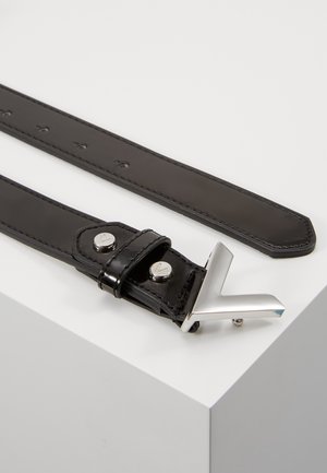 Zwarte leren riem met een zilverkleurige V-vormige gesp en twee metalen klinknagels, plat gelegd op een witte ondergrond.