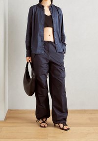 Marinblå knäppskjorta, svart crop top, lösa marinblå byxor med dragsko, svart axelremsväska och sandaler med klack och remmar.