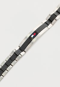 Pulsera de reloj de acero inoxidable con acentos de goma negra, que presenta un diseño trenzado clásico y un pequeño logotipo en rojo, blanco y azul.