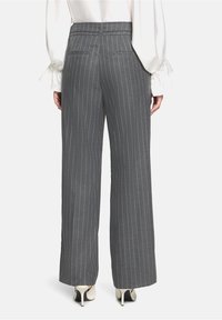 Grå pinstribet brede bukser med en tætsiddende talje og baglommer. Kombineret med en hvid bluse med flæser på ærmerne og sorte hæle.