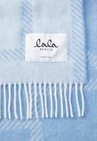 Sciarpa di lana azzurro chiaro con frange, caratterizzata da un sottile motivo diagonale e un'etichetta bianca con la scritta "lala BERLIN, made in Italy."