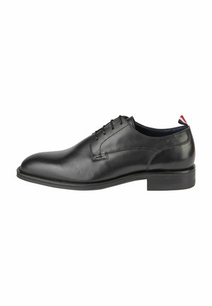 Chaussure habillée noire en cuir avec une finition lisse, un bout arrondi élégant, cinq œillets, et un design minimaliste. Semelle en caoutchouc avec un petit talon.