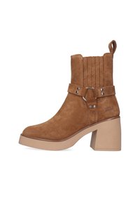 Botín de ante marrón con punta redondeada, tacón grueso de bloque y detalle de correa con hebilla. Presenta ranuras verticales en la parte superior.