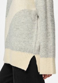 Kreemja ja halli värvi kudum-sviiter ribitekstuuriga, millel on külgsuunised ja erinevad horisontaalsed triibumustrid keha ja varrukate peal.