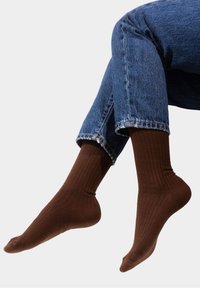 Brązowe skarpetki prążkowane z miękkiego materiału, dopasowane do kostki. Noszone z podwiniętymi niebieskimi dżinsami, eksponującymi fakturę skarpetek.