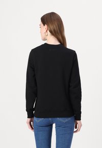 Felpa nera con maniche lunghe, scollatura a girocollo e polsini a coste. Presenta un logo discreto sulla schiena. Abbinata a jeans di denim blu.