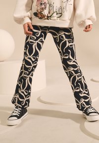 Flared pants with a navy background and white ribbon pattern, made of textured fabric. Paired with black sneakers featuring white laces.
