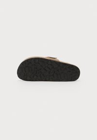 Tan sandal with a textured black rubber sole. Features a single strap with a platform, designed for comfort and stability.