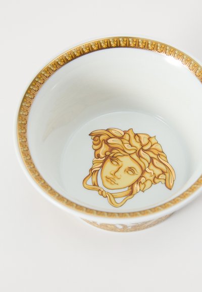 A kerek kerámia tál fényes fehér belsővel rendelkezik, közepén arany Medúza motívummal, míg a peremén díszes arany mintázattal.