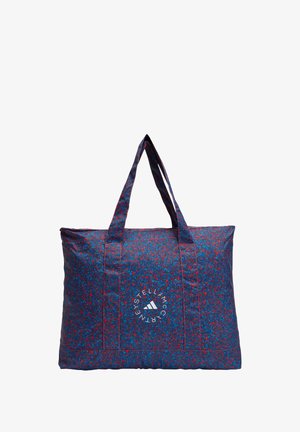 Large tote bag made of patterned fabric in blue with red splatters. Features two sturdy handles and a circular logo on the front.