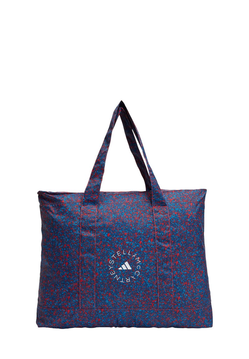 Gran bolsa de mano hecha de tela estampada en azul con manchas rojas. Cuenta con dos asas resistentes y un logotipo circular en la parte frontal.