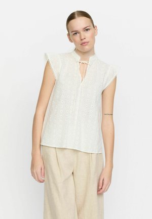 White eyelet blouse with a mandarin collar, tie detail, and short flounced sleeves. Lightweight fabric with decorative stitching and pattern.