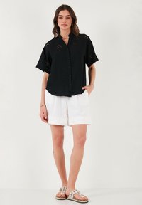 Black short-sleeve shirt with button closure and floral embroidery details, paired with white shorts and patterned sandals.