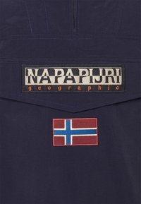 Marinblå jacka i tyg med "NAPAPIJRI geographic"-logotyp och ett Norge-flaggmärke i röd, vit och blå broderi.