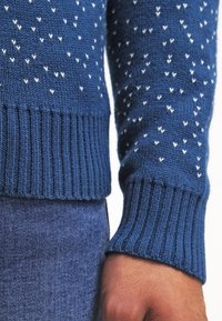 Blå stickad tröja med en texturerad mönster av små vita hjärtan, med ribbade ärmslut och nederkant, i kombination med denimtyg.