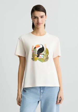 T-shirt en coton blanc mettant en avant un graphique coloré de toucan entouré de feuilles vertes et de fleurs. Manches courtes et coupe décontractée.