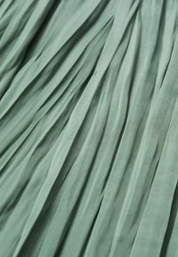 Zacht groene stof met gelijkmatig verdeelde verticale plooien die een gestructureerd, vloeibaar patroon over het oppervlak creëren.